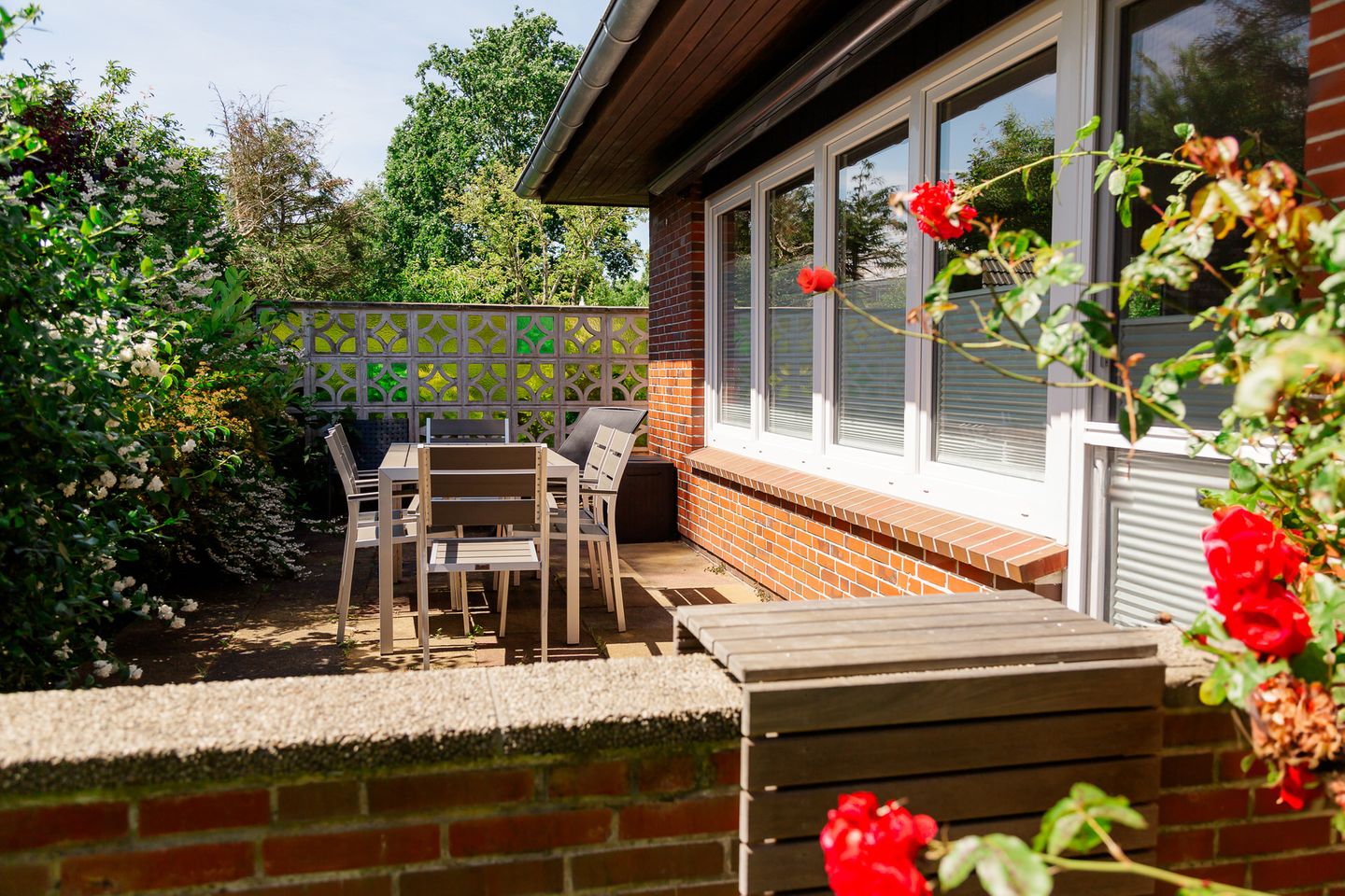 Terrasse am Haus mit Gartentisch, Stühlen, Sichtschutz und roten Rosen
