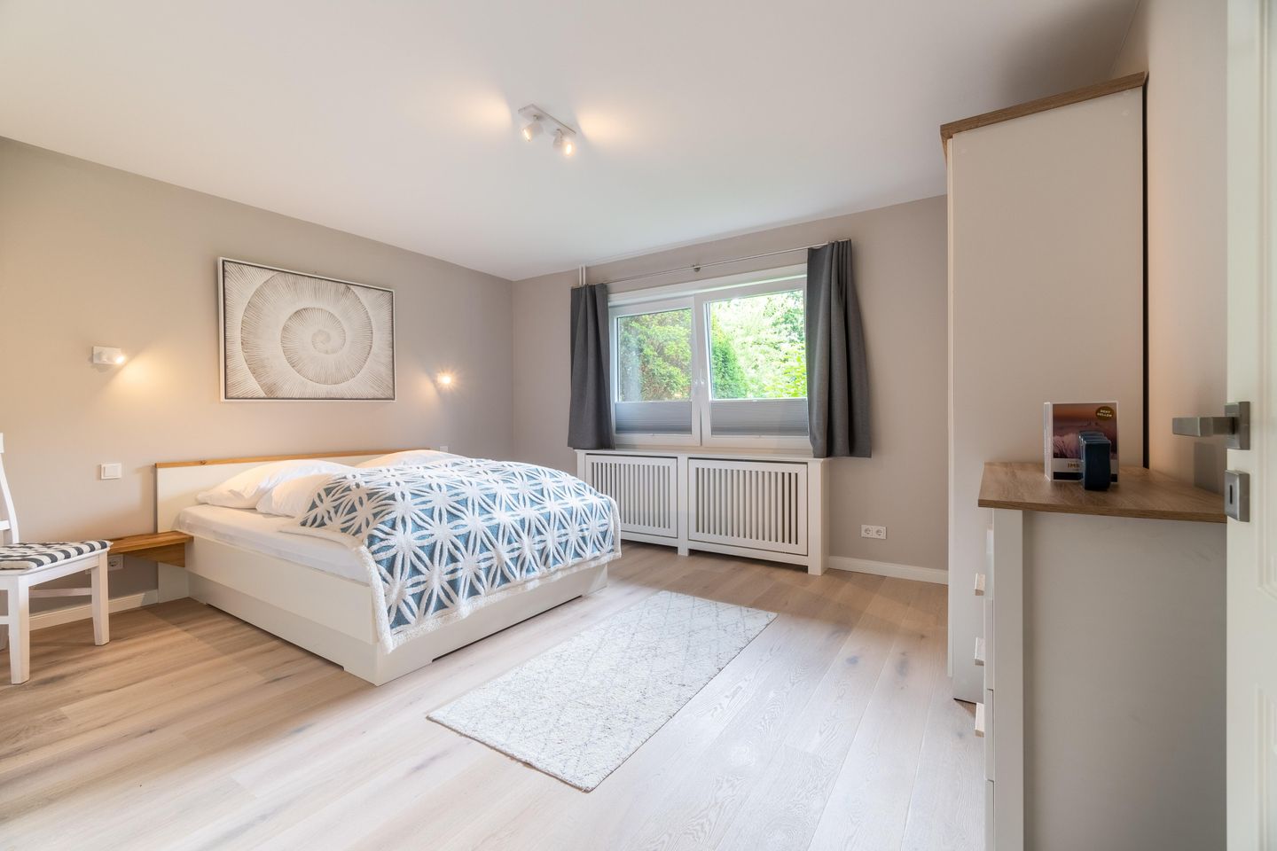 Schlafzimmer mit Doppelbett, gemusterter Bettwäsche und grauen Vorhängen